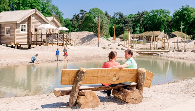 Twee volwassenen op een bankje en kinderen spelend aan het water in Efteling Loonsche Land.